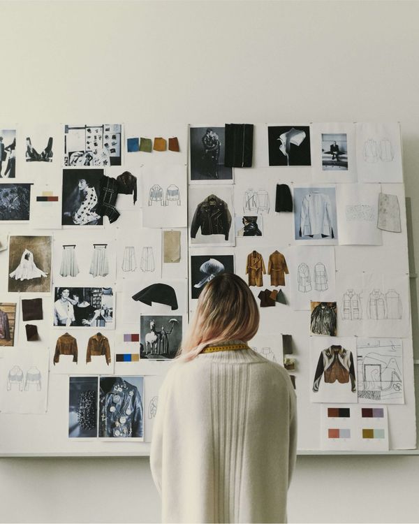 A woman is standing in front of a moodboard wall showing sketch, pictures, and inspiration drawings of leather jackets.
