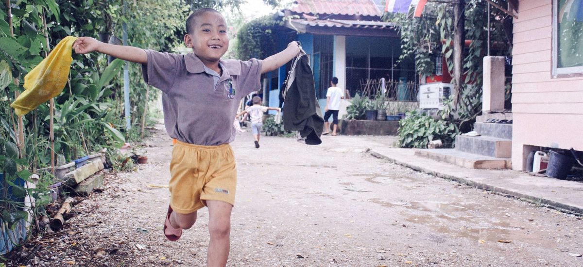 Kid running in the street with a big smile and open arms.