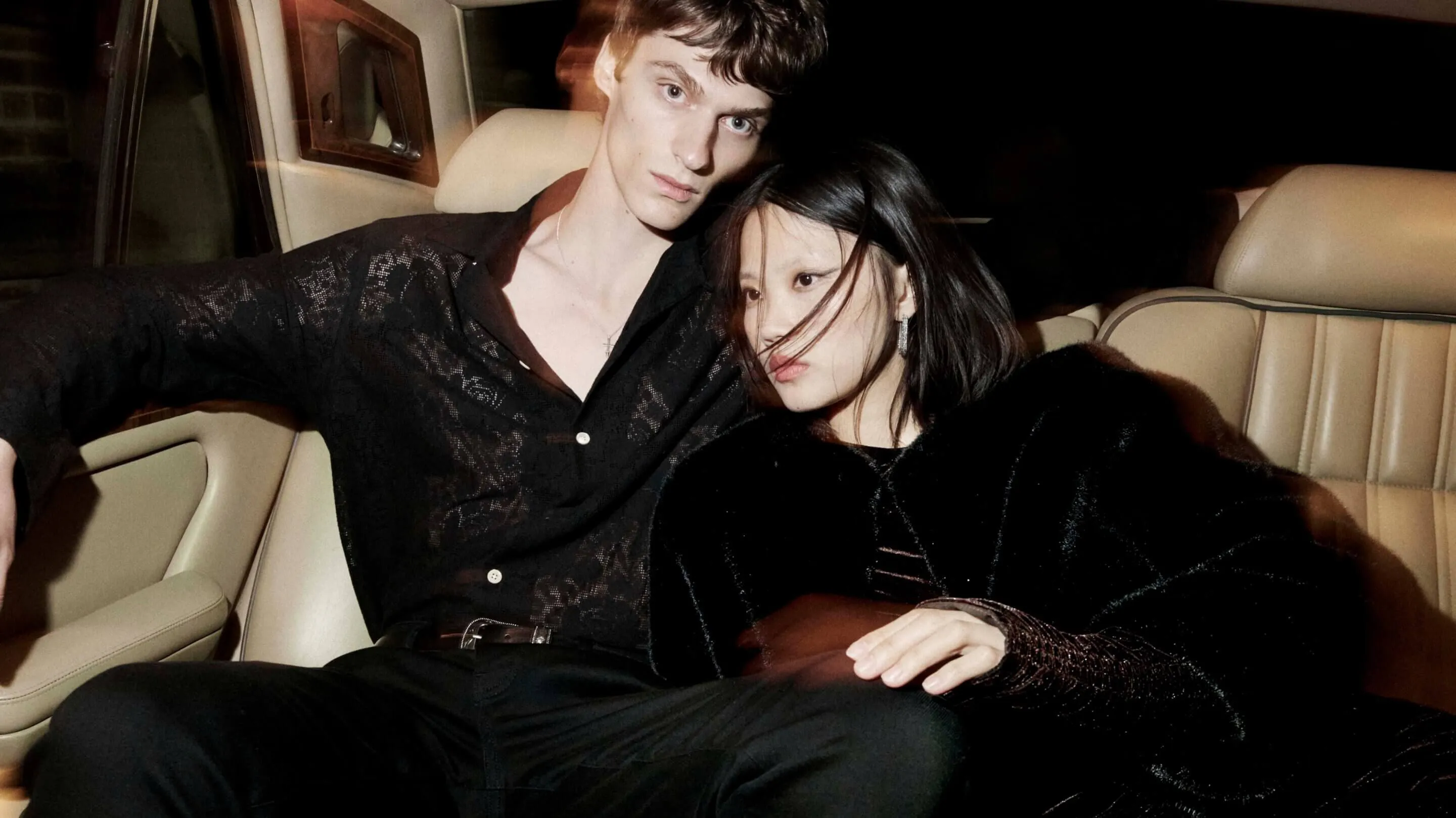 A male and female and male model sitting in the back of a car wearing black clothing.