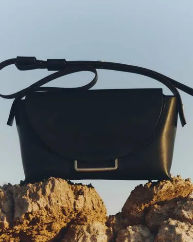 Closeup of a black leather handbag on rocks.