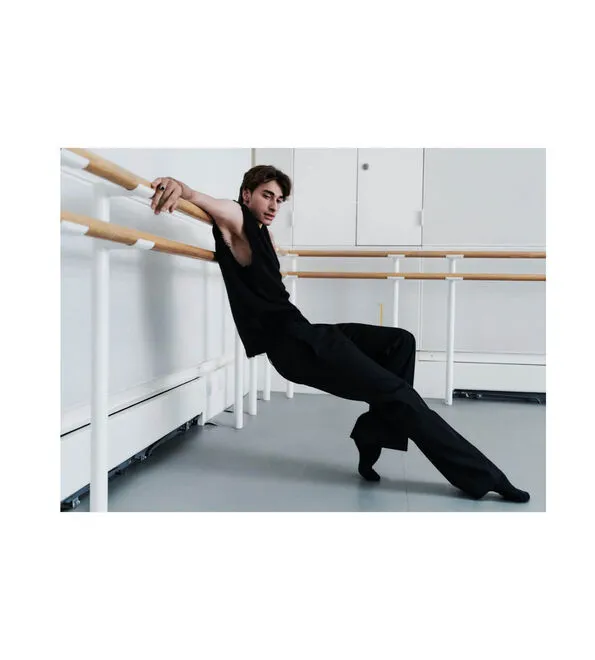 A man wearing a black vest and black trousers leaning over a barre.