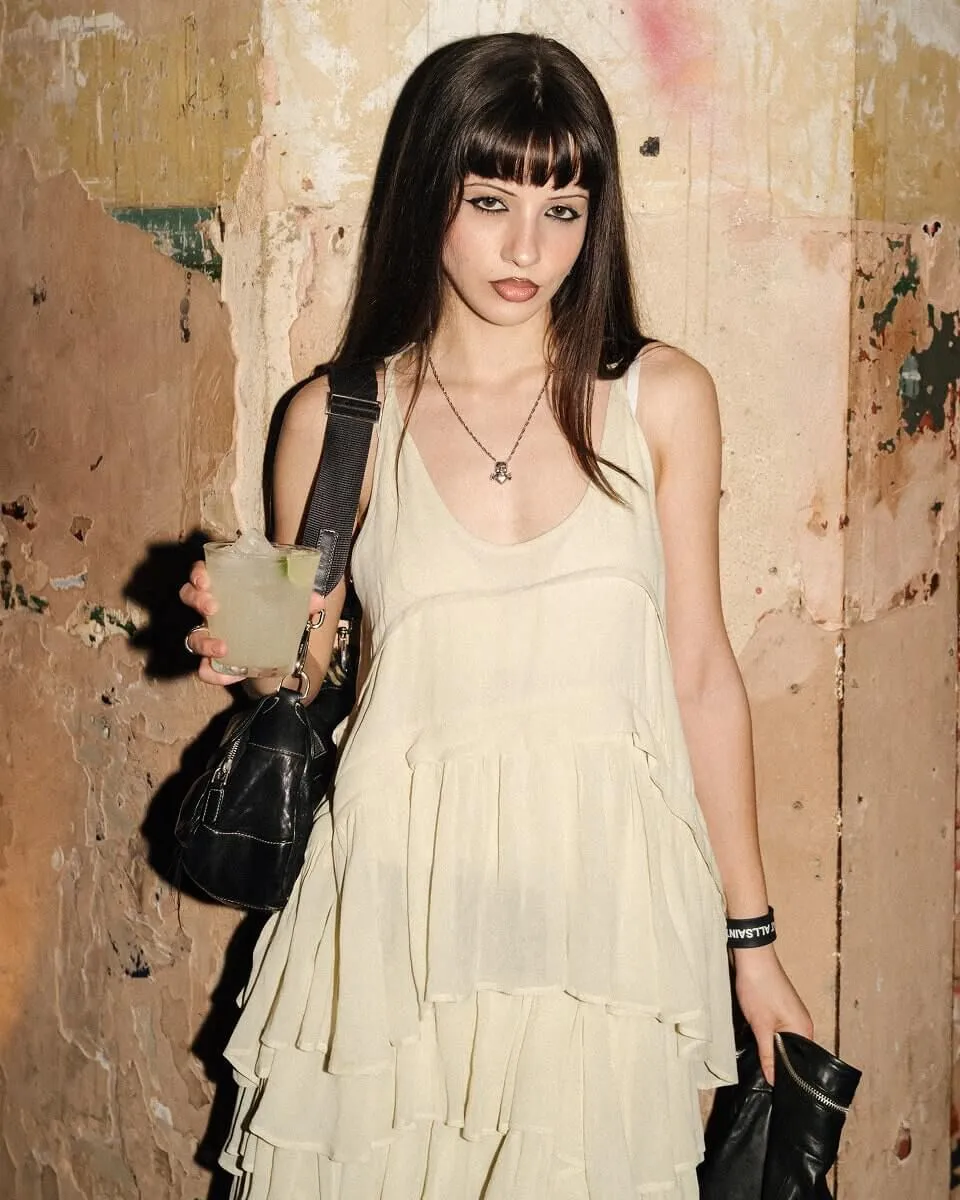 A young woman wearing the AllSaints Cavarly dress and holding a drink