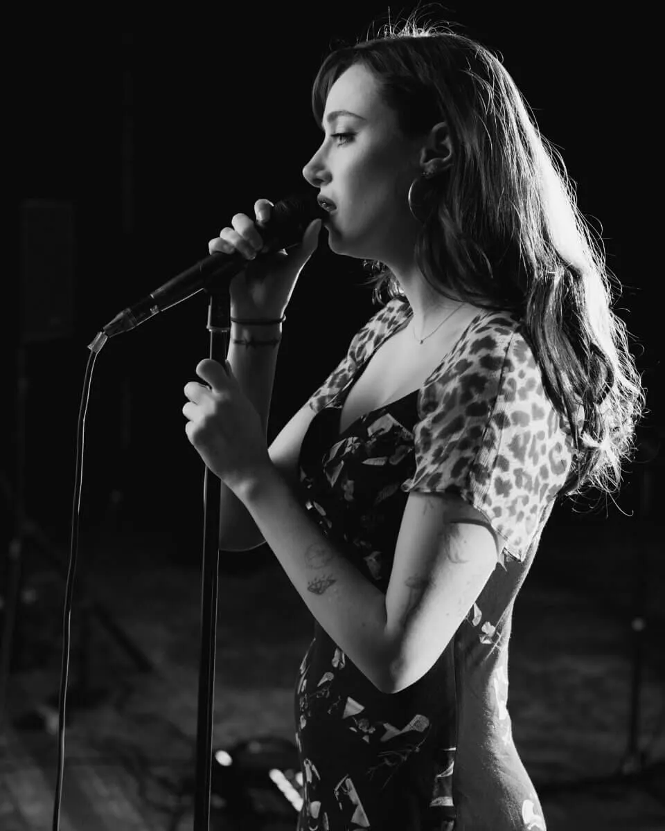 Black and white profile portrait of Olivia OBrien singing in the microphone.