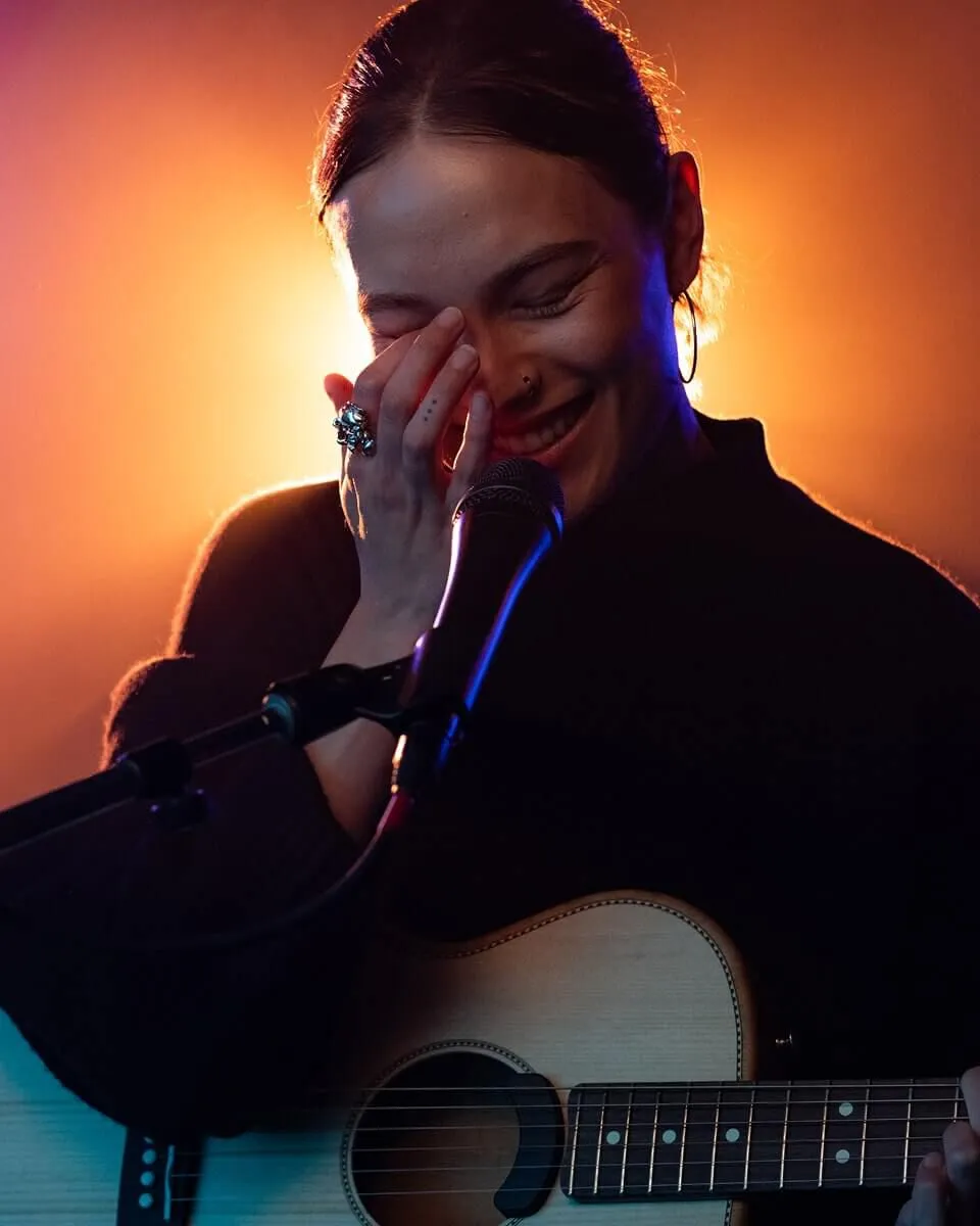 Abby on stage with a guitar laughing.
