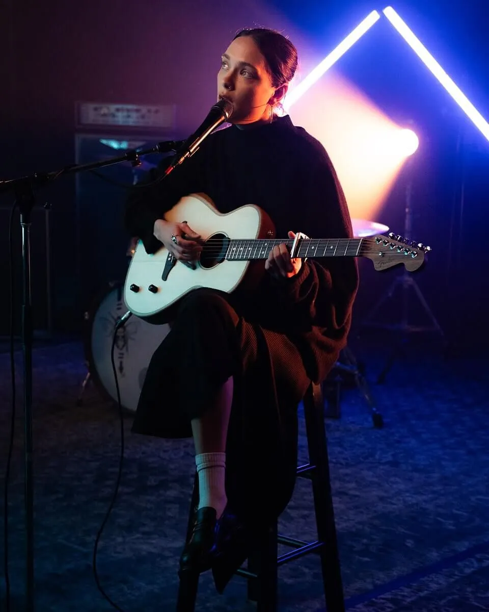 The front singer playing in front of a microphone, with yellow and purple light.