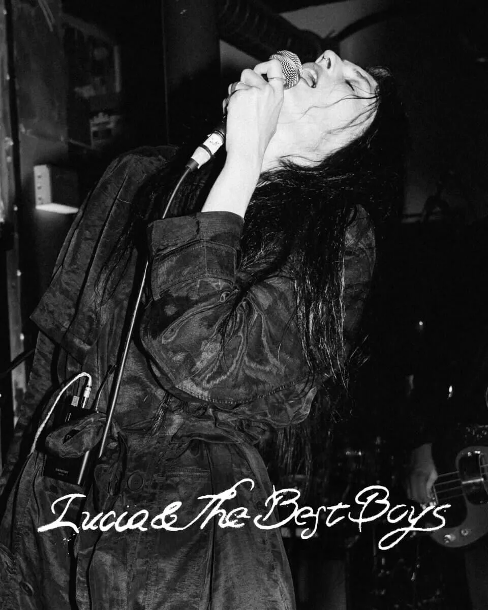 Black and white closeup shot of Lucia & The Best Boys front singer on stage singing into a microphone.