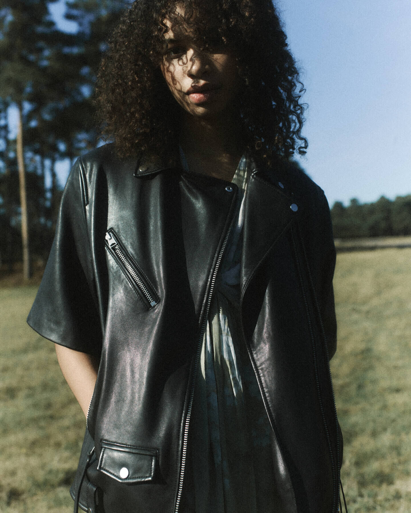 Woman wearing and black leather jacket and green dress in a field