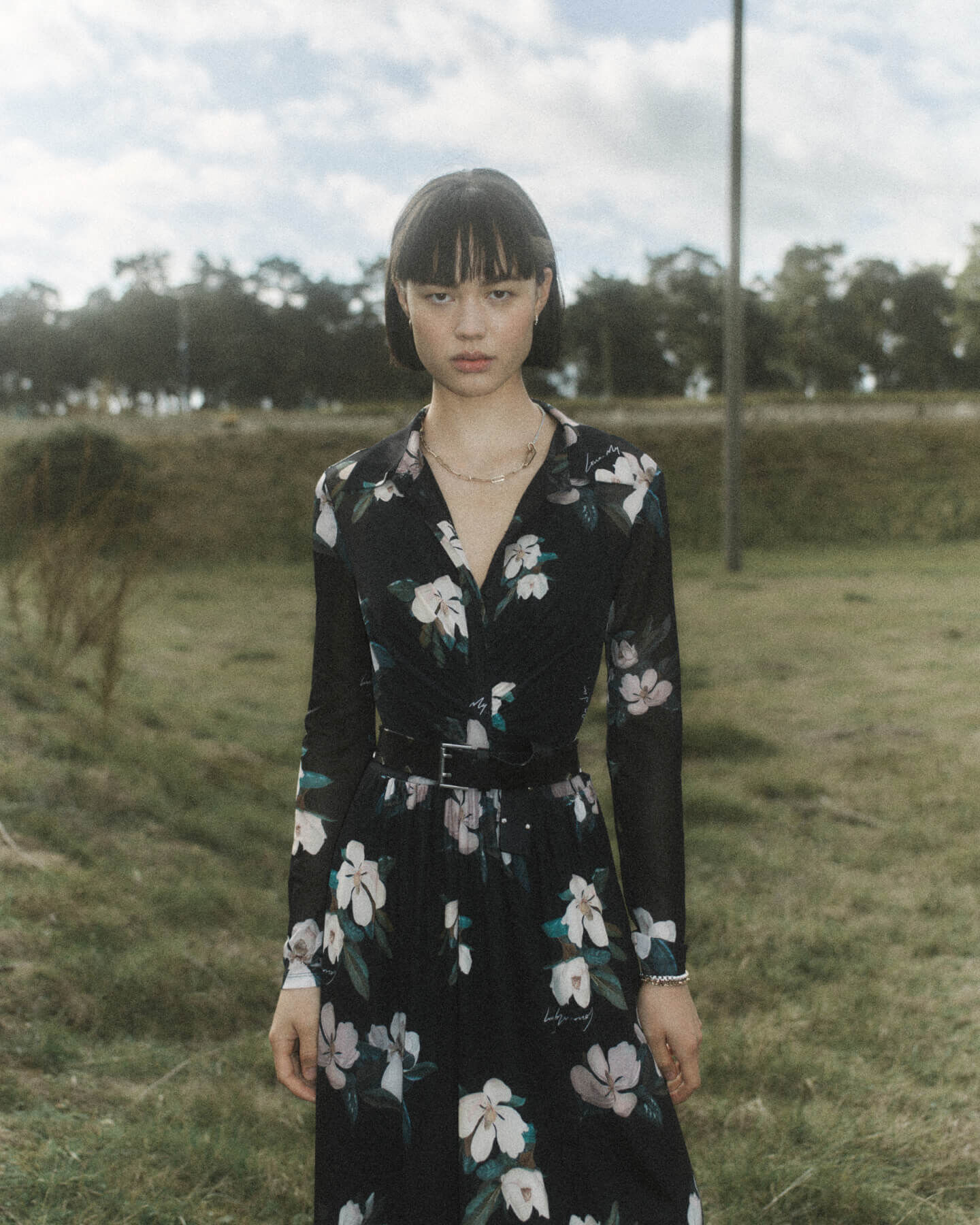 Women wearing a black floral dress with black leather belt and silver jewellery in a field