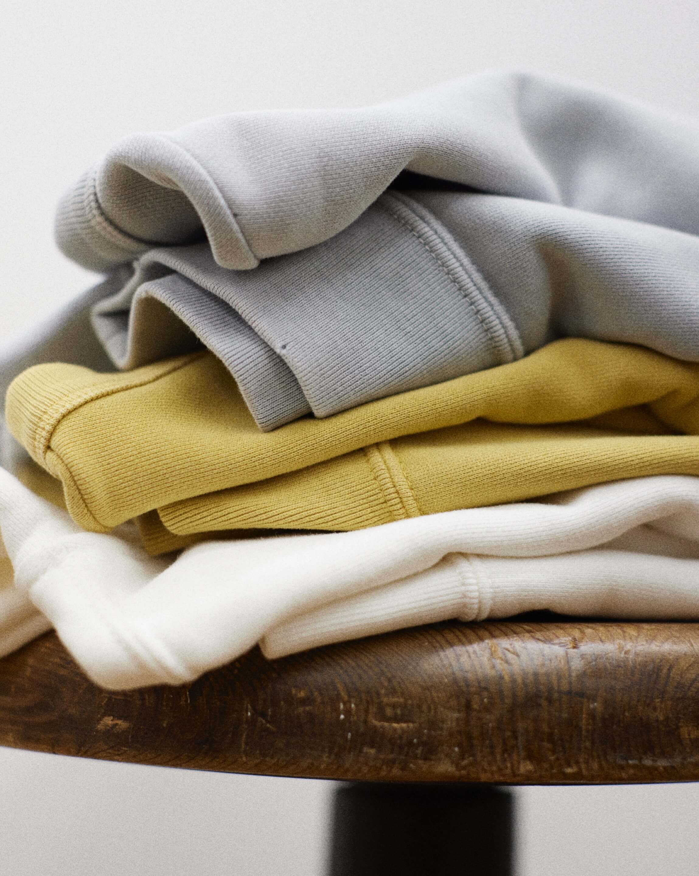 Pile of sweatshirts folded on a wooden stool.