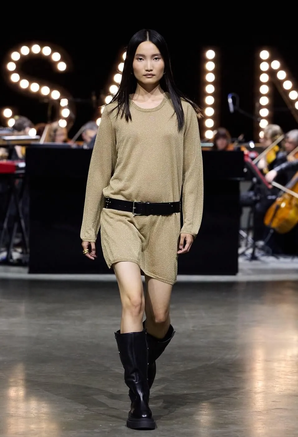 Woman wearing sparkled gold dress with black belt and black boots