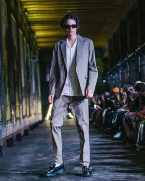 A man wearing a grey suit and black brogues catwalking.