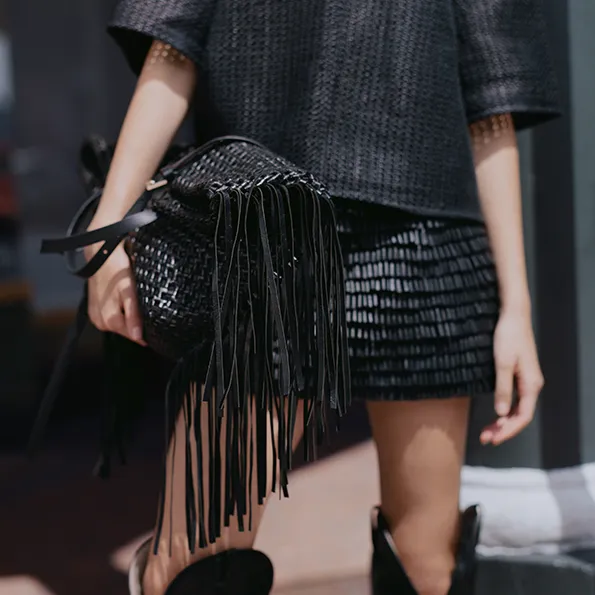 Woman wearing a beige suede shirt and holding a black leather bag.