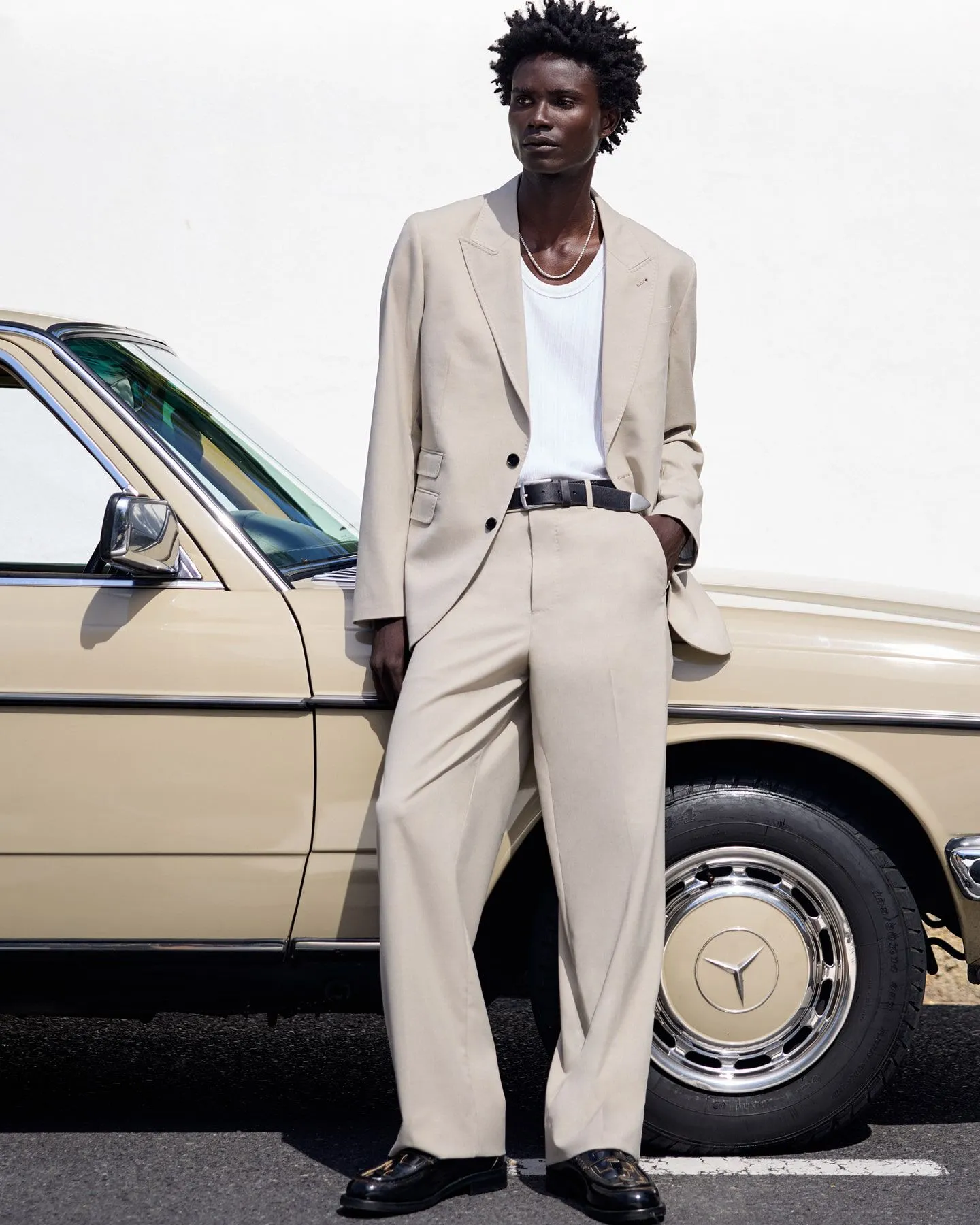 Photograph of male model in beige suit infront of a car.