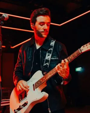 A guitarist plays electro guitar and wears a biker jacket.