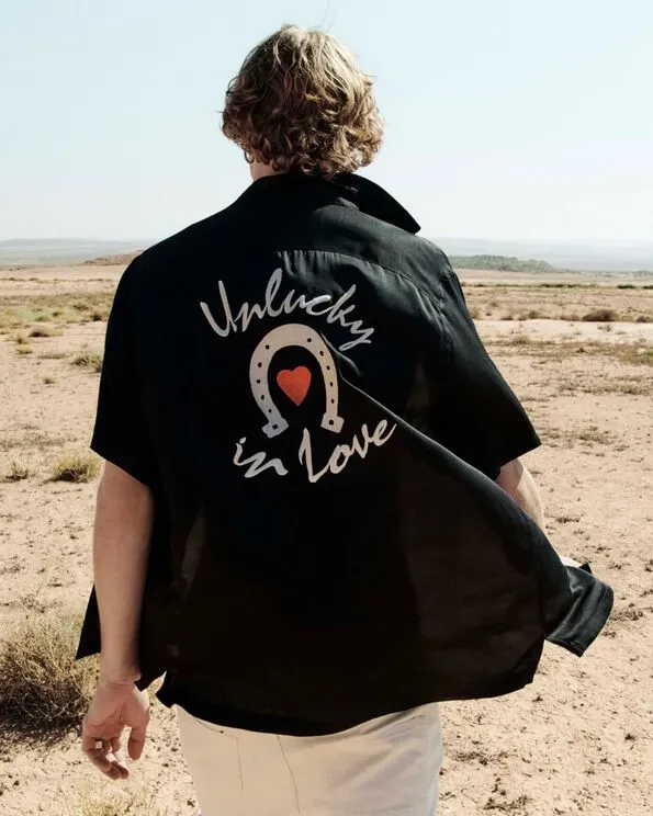 Black and white photograph of a man wearing an open black shirt, black AllSaints boxers and white jeans walking in the desert.