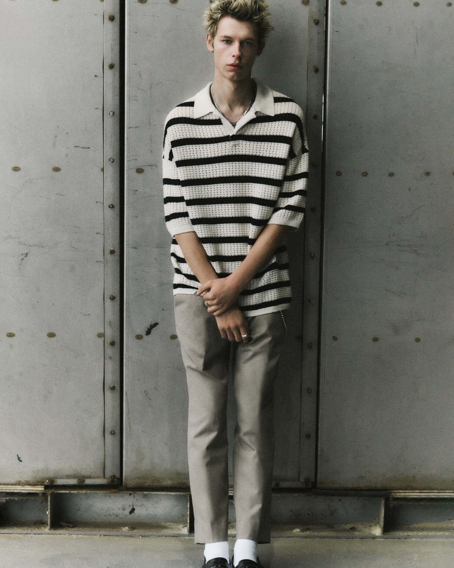 Man wearing a black and white striped knitted polo with grey chinos.