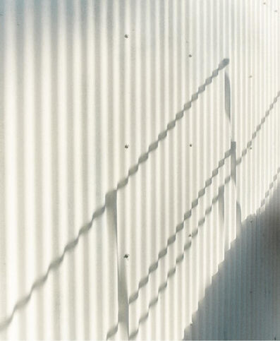 Shadow of a metallic structure on a white corrugated iron wall