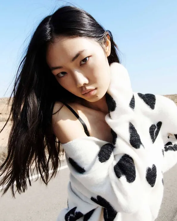 Portrait of a model wearing a white cardigan with black hearts motif standing on the road.