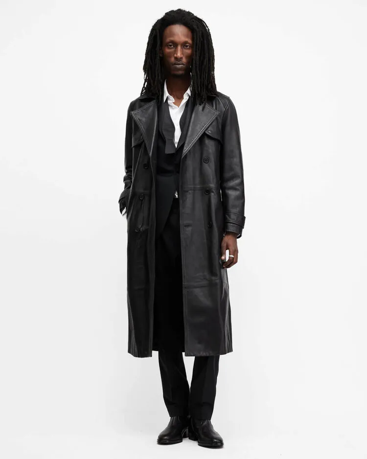 A man wearing a long black leather trench coat and black trousers.