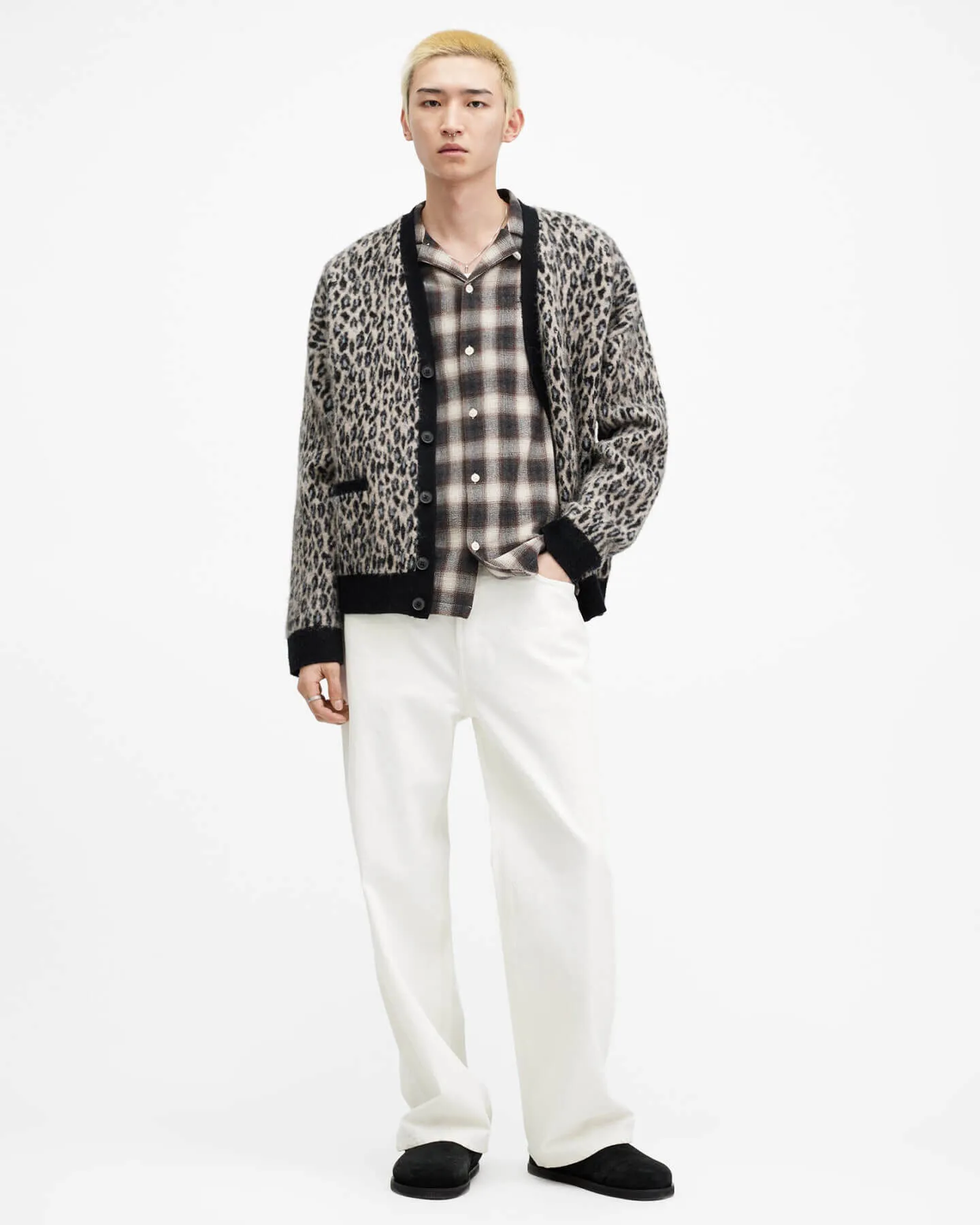 Man wearing a leopard patterned cardigan over a checkered brown shirt, with white wide leg jeans.