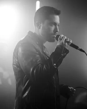 Jordy singing into a microphone wearing a leather jacket